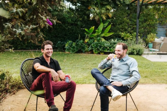 Two people sitting in a garden, one holding a HOPWTR can